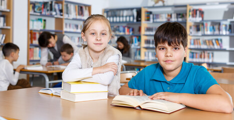 Fototapeta na wymiar Portrait of two school children preparing for lesson in school library, reading textbooks together