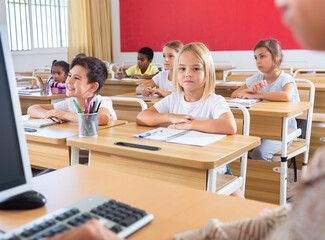 Group of focused pupils sitting at classroom working at class with teacher, looking at board