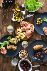 Snack dinner table concept. Bruschetta with ham, cheese, baked potatoes, olives and olives with wine top view