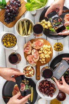 Friends take pictures of what they eat. Snack dinner table concept. Bruschetta with ham, cheese, baked potatoes, olives and olives with wine top view