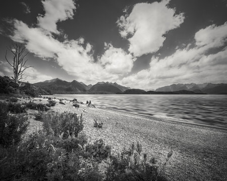 Beautiful view of Lake Manapouri in black and white with the mountain in the distance and people walking along the lakeshore in Fiordland National Park, New Zealand, South Island.
