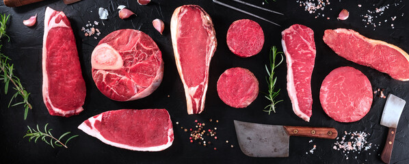 Meat cuts panorama. Raw beef pieces, shot from the top with herbs and seasoning, on a black background - obrazy, fototapety, plakaty