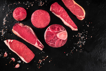 Raw meat cuts with salt and garlic, overhead flat lay shot on a dark background with copy space