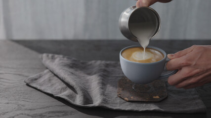 man pour steamed milk into blue cup making cappuccino
