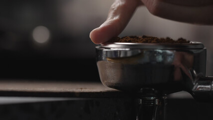 man spreading freshly ground coffee in portafilter before tamping