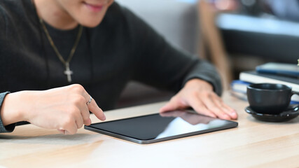 Cropped shot of smiling young man sitting in living room and using digital tablet.