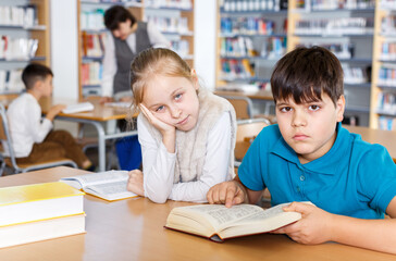 Portrait of tired girl and boy sitting with open books in school library, preparing for lesson