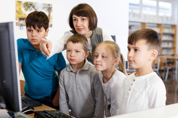 Friendly female teacher giving lesson to interested school kids in computer class