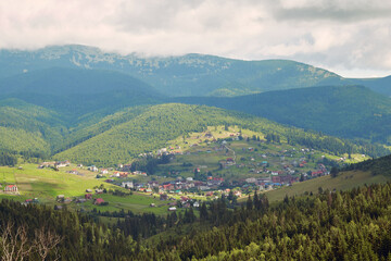 Fototapeta na wymiar Small mountains village with meadows rolling through forested hills. Carpathians mountains with beautiful summer weather