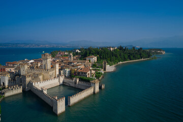 Fototapeta na wymiar Amazing view to the old bridge and harbor of Sirmione. View by Drone. Rocca Scaligera Castle in Sirmione. Aerial view on Sirmione sul Garda. Italy, Lombardy.