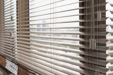 Aluminum blinds on the office windows. Made from metal. Venetian blinds closeup on the window. Silver color. City landscape is in the background. Modern sun protection and window decoration. Selective