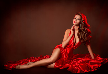 Sexy Woman Red Dress Fashion. Sensual Model lying in Slit Gown. Evening Make up and curly wavy Hairstyle. Copy Space