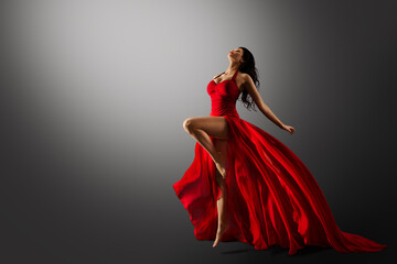 Dancer in Red Dress Jumping. Woman Ballerina Expressive Balance Dance Flying Fabric in Air. Fashion Model Dancing over Gray Studio Background