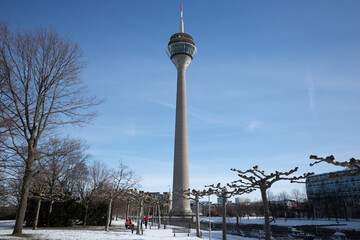 Obraz premium Outdoor sunny view of Rheinpark Bilk covered by snow and background of Rhine Tower in Düsseldorf, Germany. 