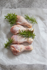 Raw chicken drumsticks with rosemary on greaseproof paper. Concrete background