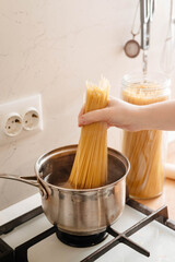 Woman puts a portion of spaghetti in a saucepan to cook
