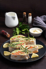 Rolls of thin pita bread and red salted salmon with lettuce leaves on a black ceramic plate, dark wooden background. Copy space.
