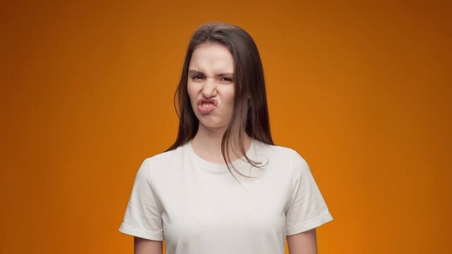 Young woman expressing aversion, rejection, negative attitude against yellow background