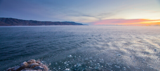 The distant shore and the blue water of Lake Baikal clogged with fine ice at a cold dawn - 417293593