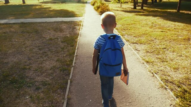 schoolboy boy goes through the park with a backpack and a textbook to school. kid dream education study concept. school boy going to school. schoolboy kid going home through the park fun dream