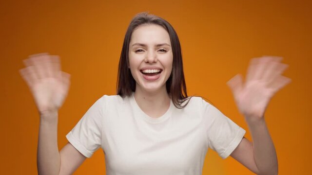 Young woman smiling and shaking hand, greeting someone, against yellow background