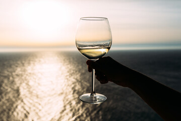 Hand holding glass of wine over the sea. Romantic vacation. Hand holding a glass of wine against the sea. Meeting the sunset with wine by the sea. Copy space