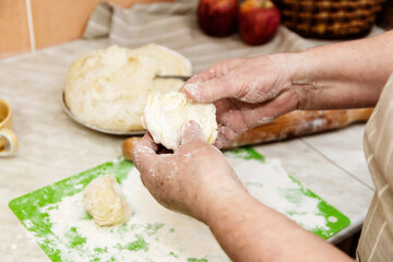 The concept of baking in home conditions. Close-up of the elderly woman's hands knead the dough.
