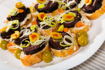 Traditional Spanish blood sausage served on fresh baguette with green olives and sliced leeks