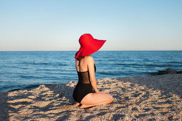 A girl in a red hat sits on the beach of the sea coast.