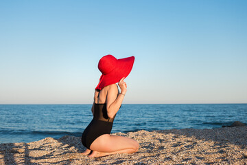 A girl in a red hat sits on the beach of the sea coast.