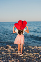 A girl in a red hat stands on the beach of the sea coast.