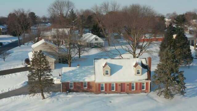 Descending aerial of cape cod house. Home in peaceful winter snow establishing scene. Snowy cold setting.