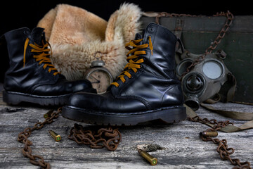 Leather boots with rusted chains and bullet shells with military gas mask and fur coat in background resting on wooden table