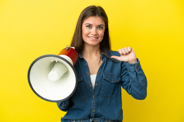 Young caucasian woman isolated on yellow background holding a megaphone and proud and self-satisfied