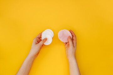 Female hands holding simple cotton pads and reusable soft pad on yellow background.