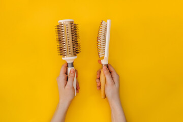 Female hands holding two hairbrushes, round and simple, on yellow background.