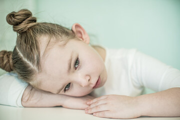Little beautiful sad girl sits at a table. High quality photo