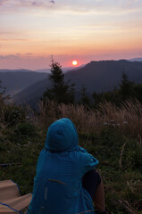 A woman greets the sunrise in the mountains. Meeting the dawn on the hill. Romantic view of the landscape in morning. A girl who looks at the mountains and sun. Mist rises from the valleys and forest