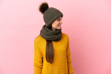 Young caucasian girl with winter hat isolated on pink background looking side