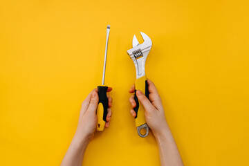 Female hands holding a wrench and a screwdriver on yellow background.