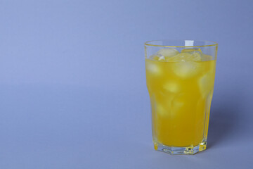 Glass of orange soda with ice cubes on violet background