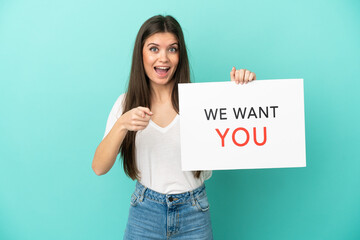 Young caucasian woman isolated on blue background holding We Want You board and pointing to the...