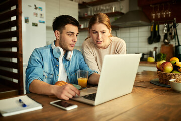 Young couple talking while using laptop at home.