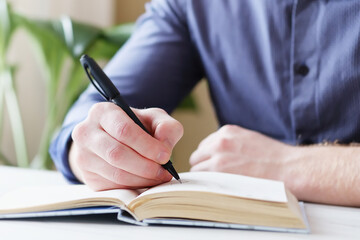 A man writes notes in a notebook with a pen - A man's hand makes a note in a notebook is shown in close-up and the background is blurred - The concept of learning and organization in personal life