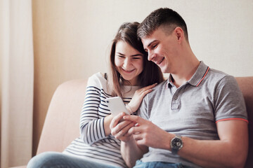 A couple of young people smiling and looking at the phone in an embrace - A man and a woman are using modern technologies - Isolation and quarantine lifestyle