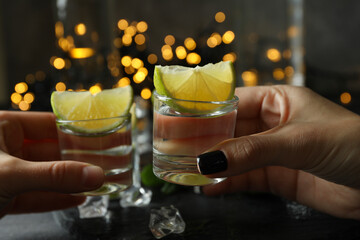 Female hands cheers with shots of vodka against blurred lights