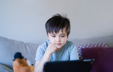Happy kid having fun watching cartoon or play game on tablet,School boy using digital pad searching the ideas on internet for his homework, Home schooling, Home learning or E-learning online education