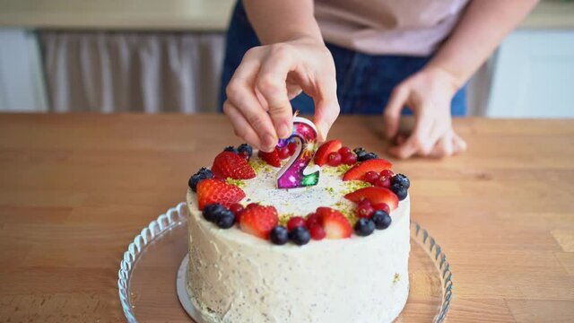A woman in the kitchen puts a candle in the shape of the number 2 on the cake