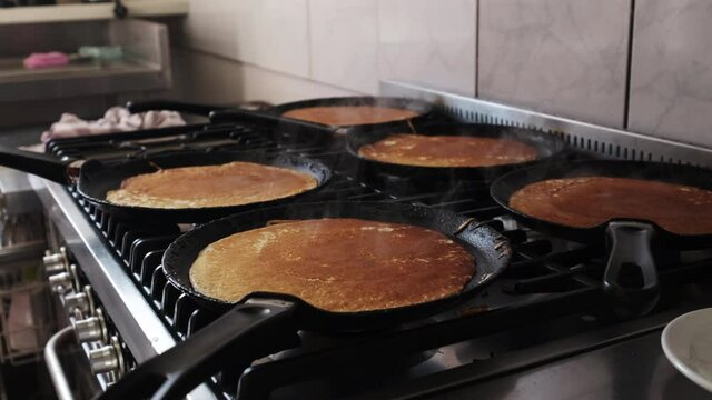 Dolly forward on pankakes being cooked on the pans of a gas oven
