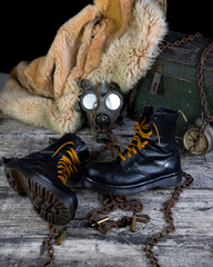 Leather boots with rusted chains and bullet shells with military gas mask and fur coat in background resting on wooden table